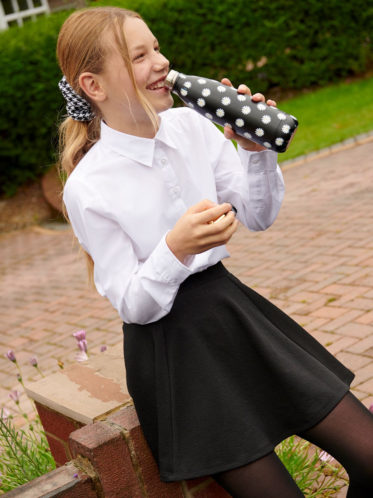 Girl in her school uniform drinking from her black daisy water bottle.