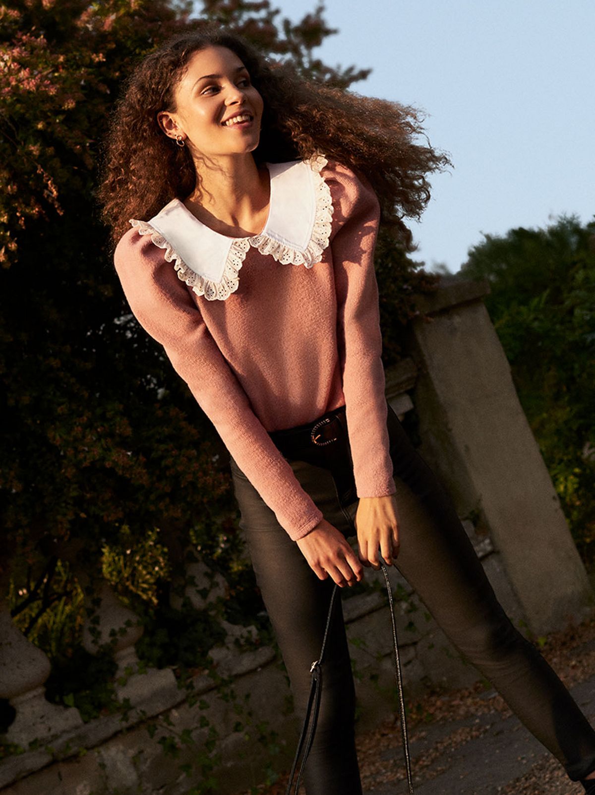 Woman leaning forward, wearing black leather-look skinny jeans and pink knit frill collar top