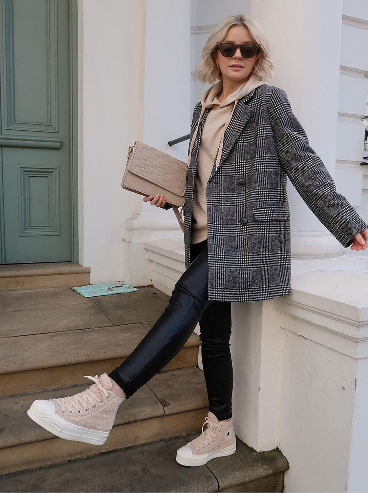 woman standing on stairs, wearing check blazer, cream hoodie and leather look trousers