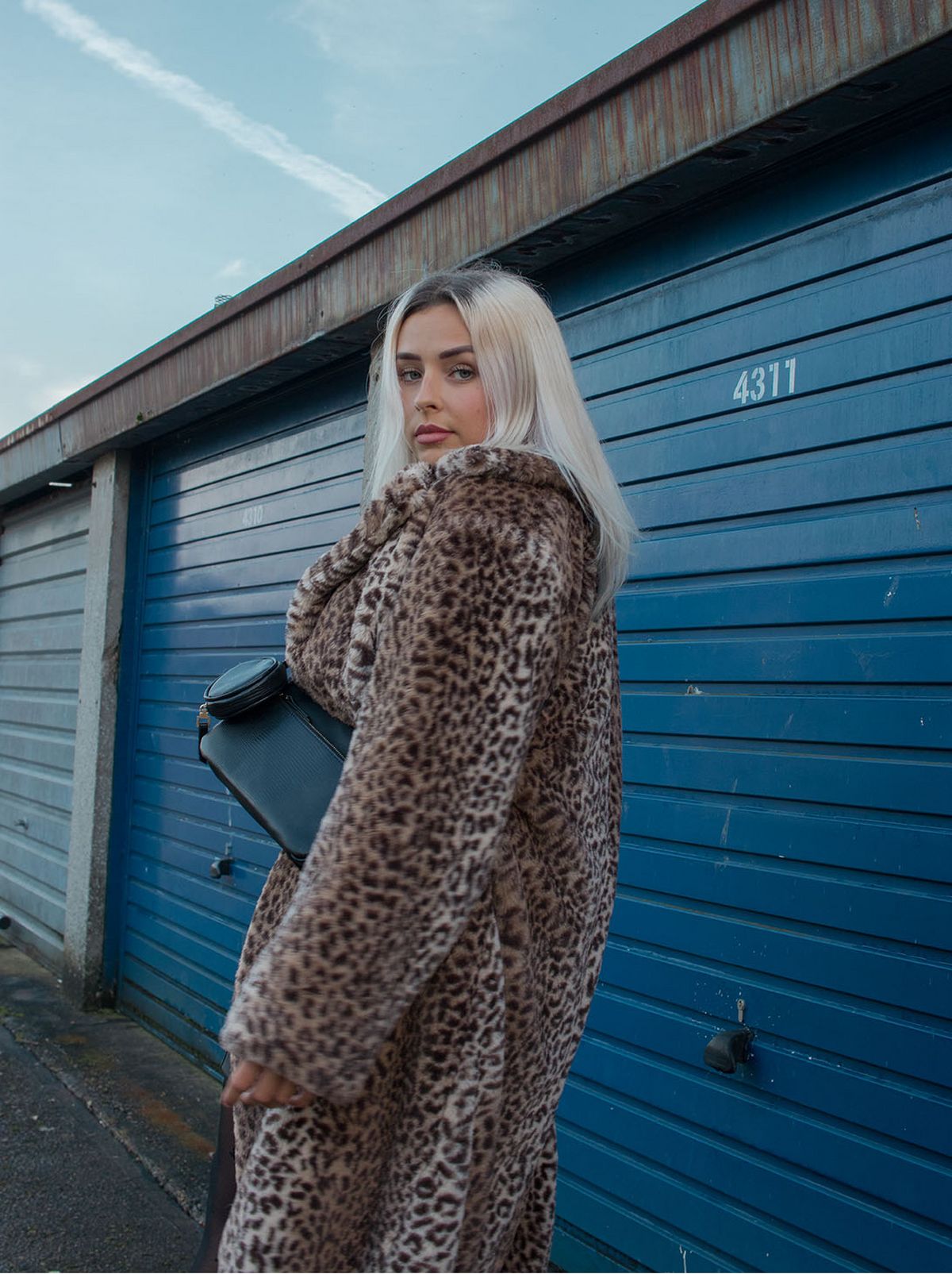 woman standing next to garages, wearing leopard print coat
