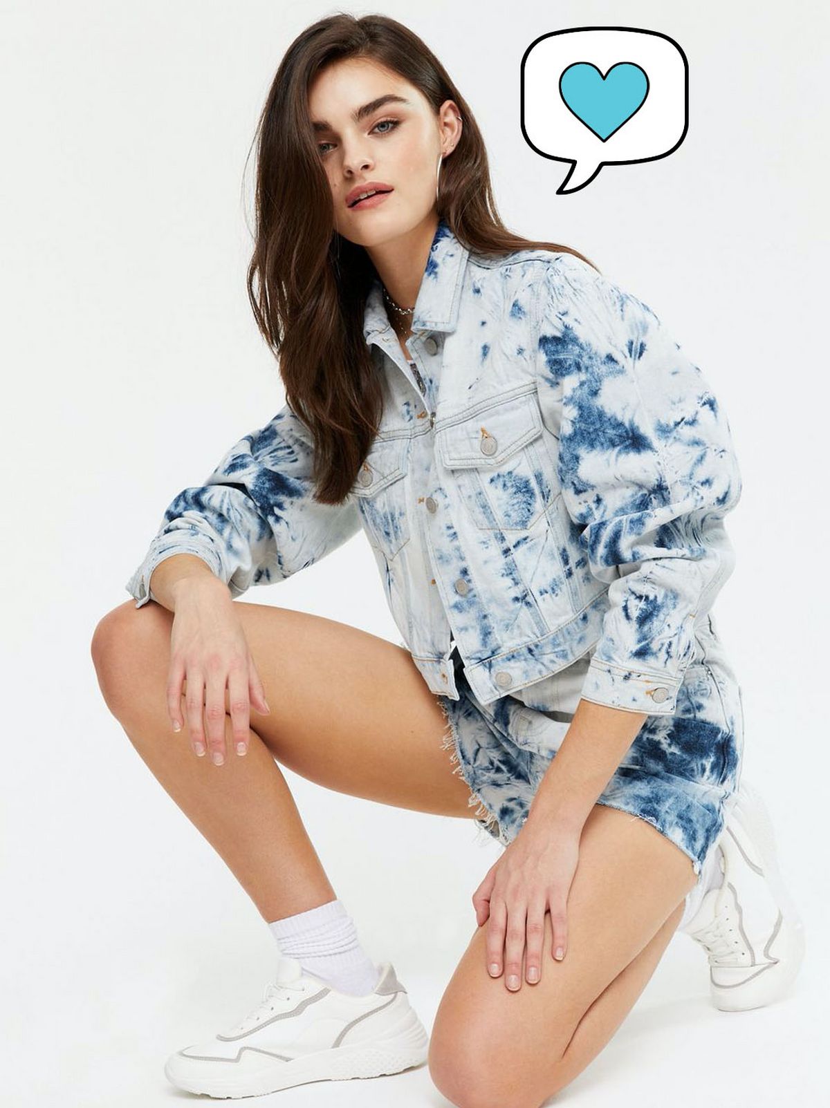 Woman wearing a blue tie dye denim crop jacket and matching shorts with white trainers
