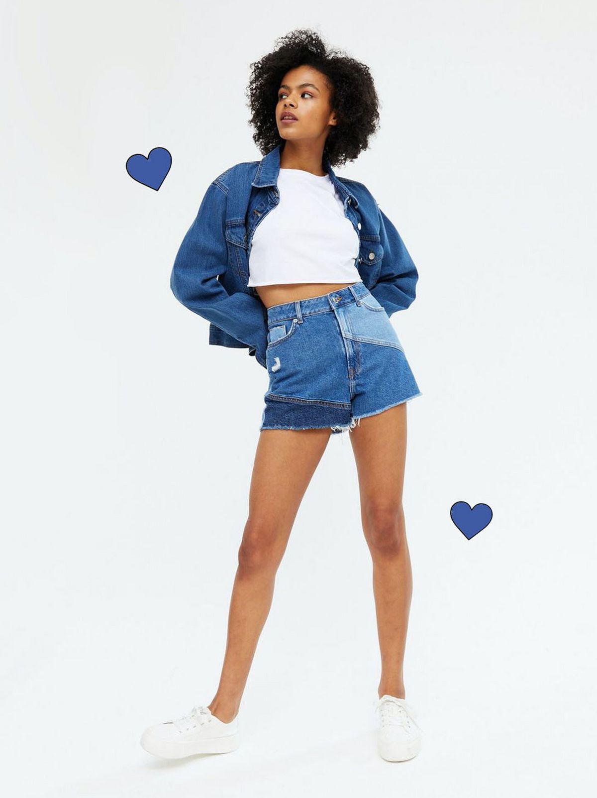 Woman wearing blue spliced denim shorts, white top, blue jacket with white trainers
