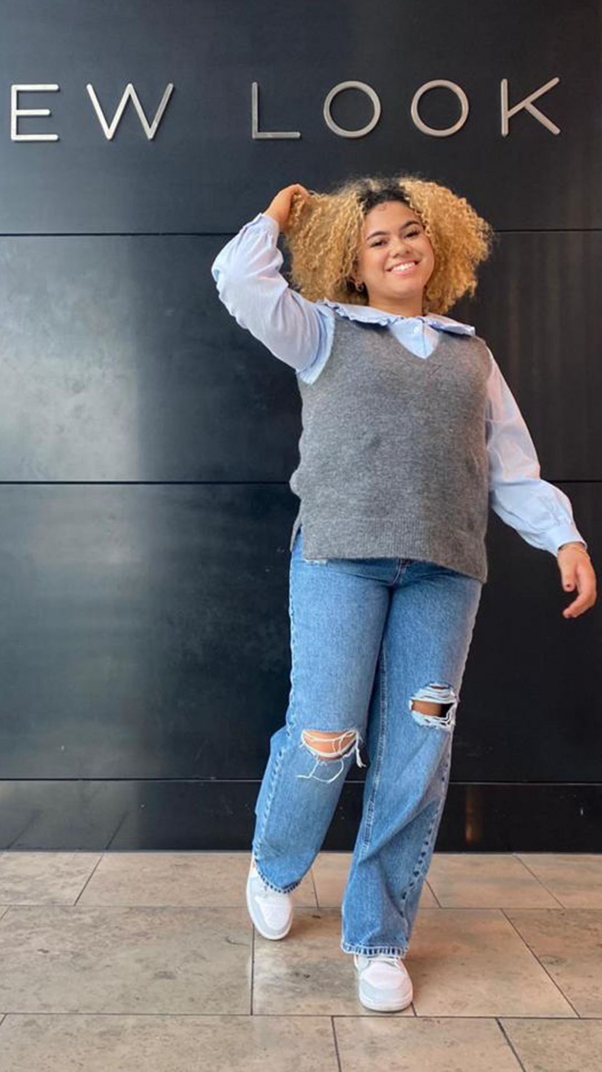 Kayleigh Plummer, Sales Advisor at New Look Stratford wearing a blue blouse, grey sweater vest and blue ripped jeans