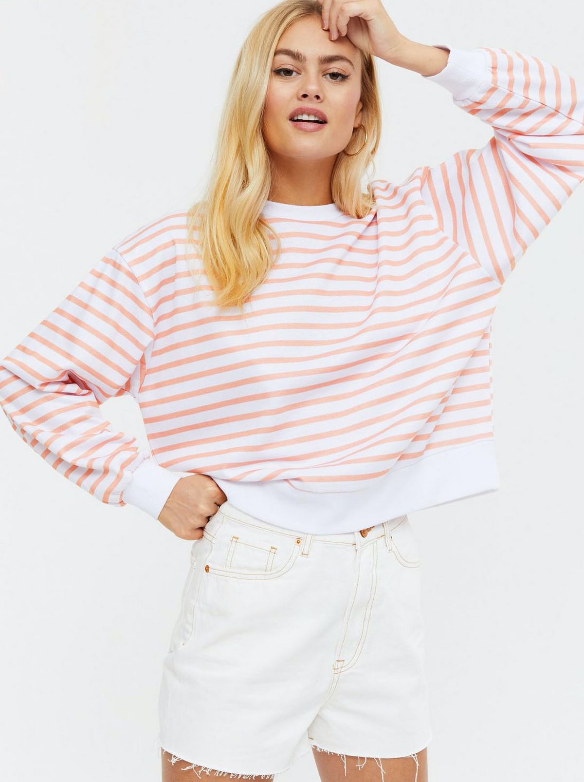 Woman wearing a orange stripe puff sleeve sweatshirt and white denim shorts