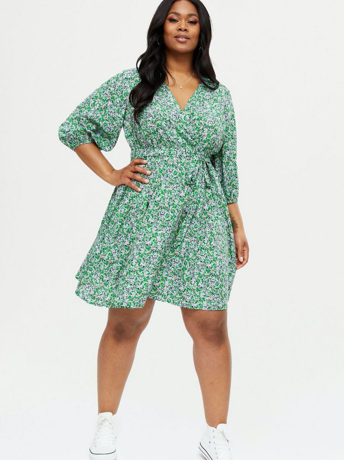 Woman wearing a green floral wrap dress and white trainers
