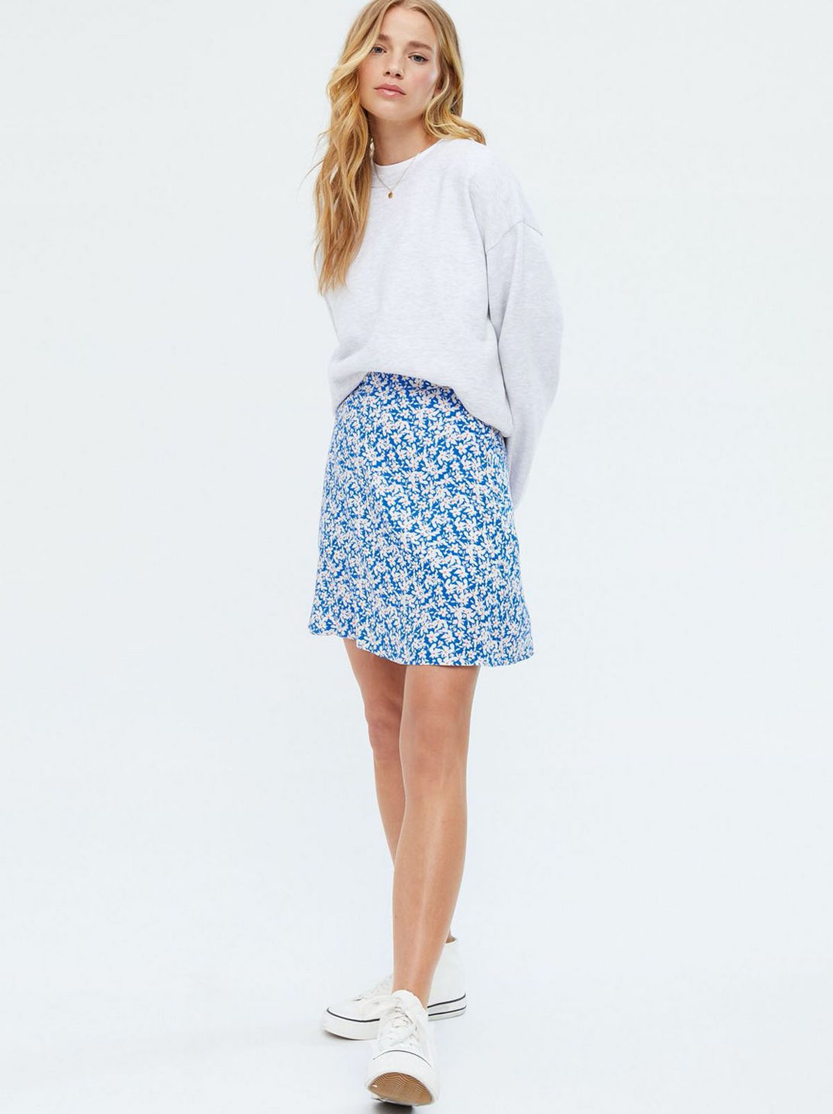 Woman wearing a floral mini skirt in blue, white jumper and trainers