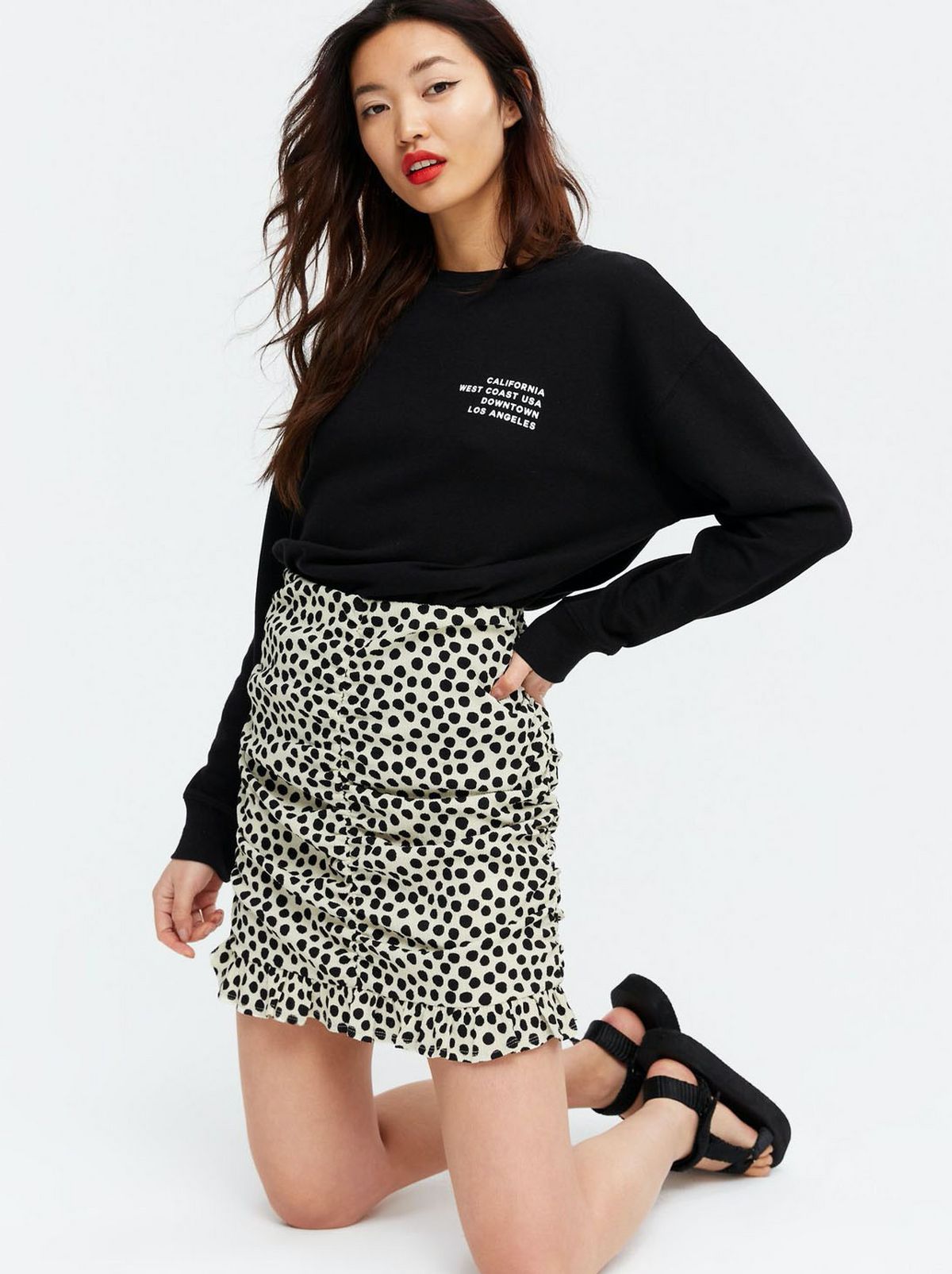 Woman wearing a white spot ruched mini skirt and black jumper and sandals