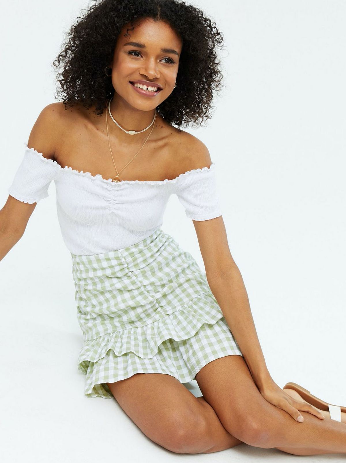 Woman wearing a green gingham mini skirt and white off the shoulder top
