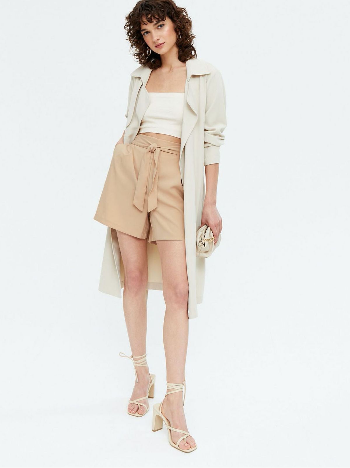 Woman wearing tie front shorts, white crop top, jacket and heels