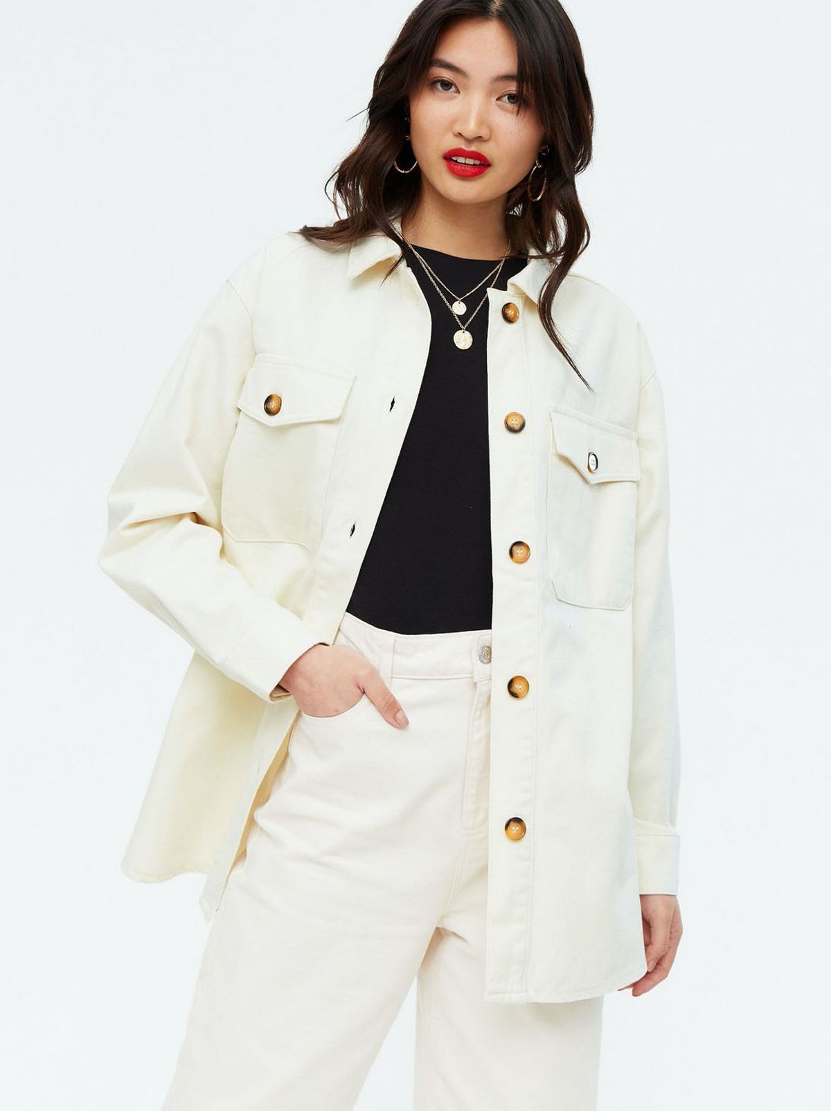 Woman wearing a cream shacket, black top and white jeans