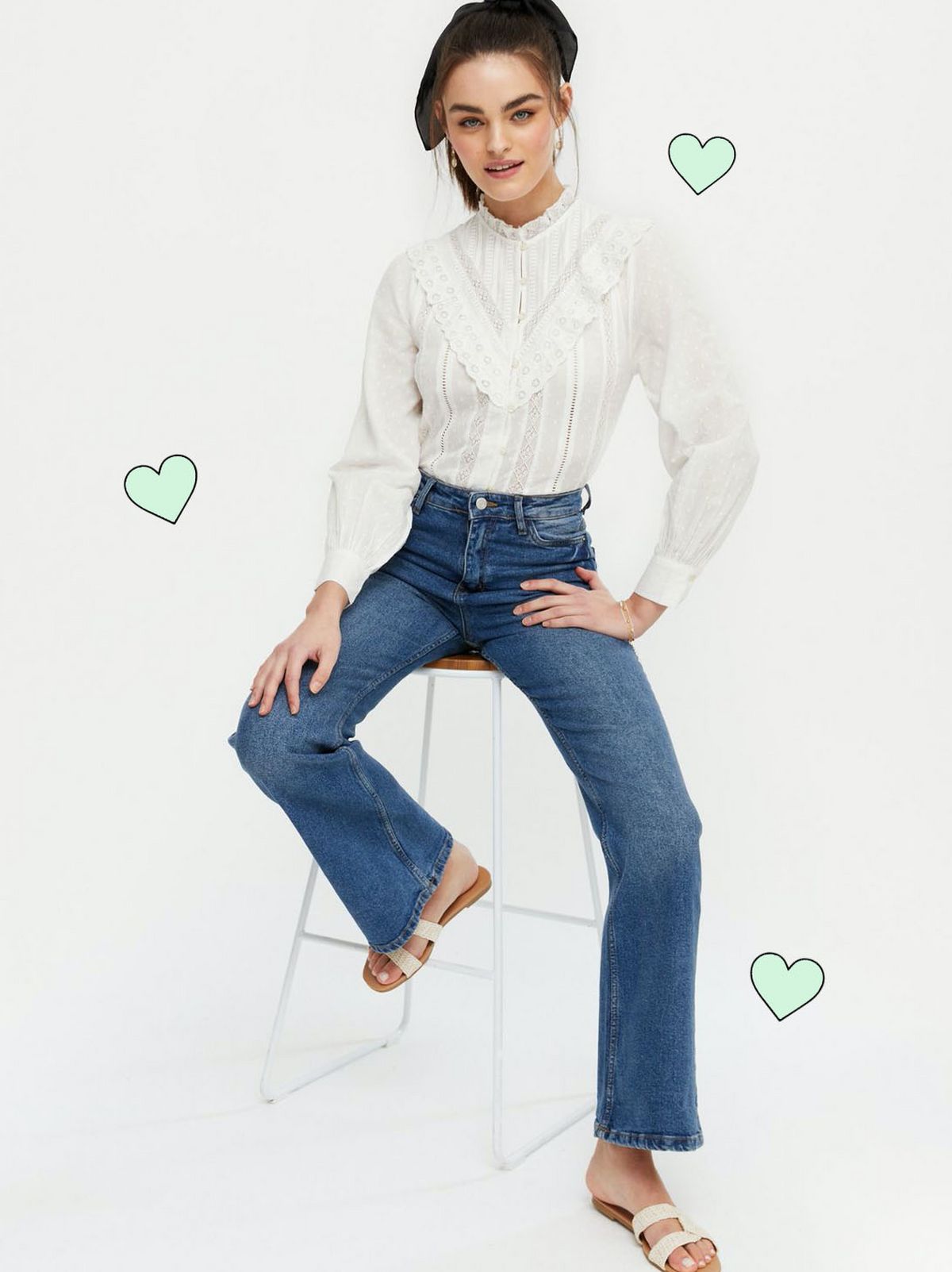 Woman wearing an off white high neck shirt, blue jeans and sliders