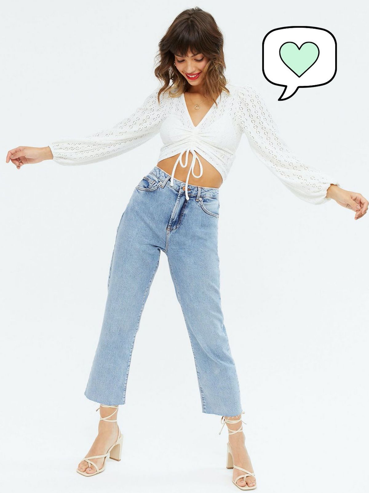 Woman wearing a cream drawstring crop top, blue jeans and heels