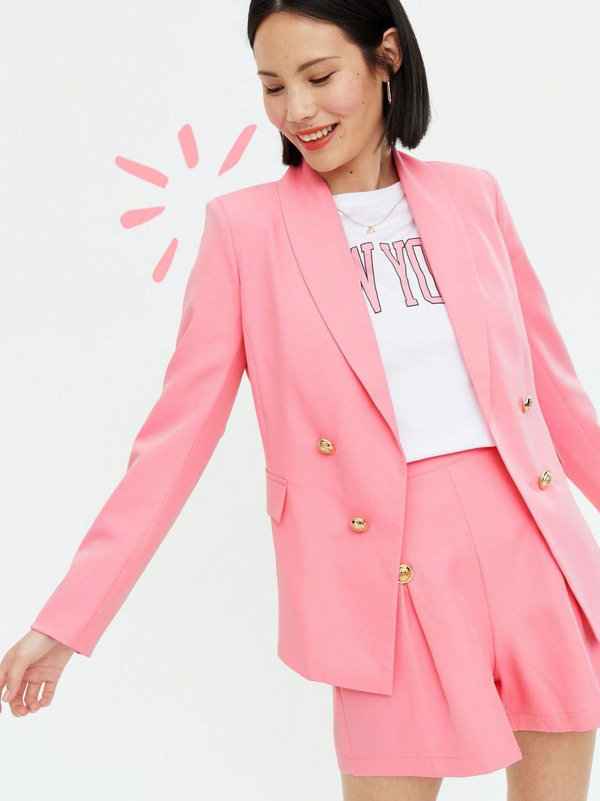 Woman wearing a pink utility button blazer, matching shorts and logo t shirt