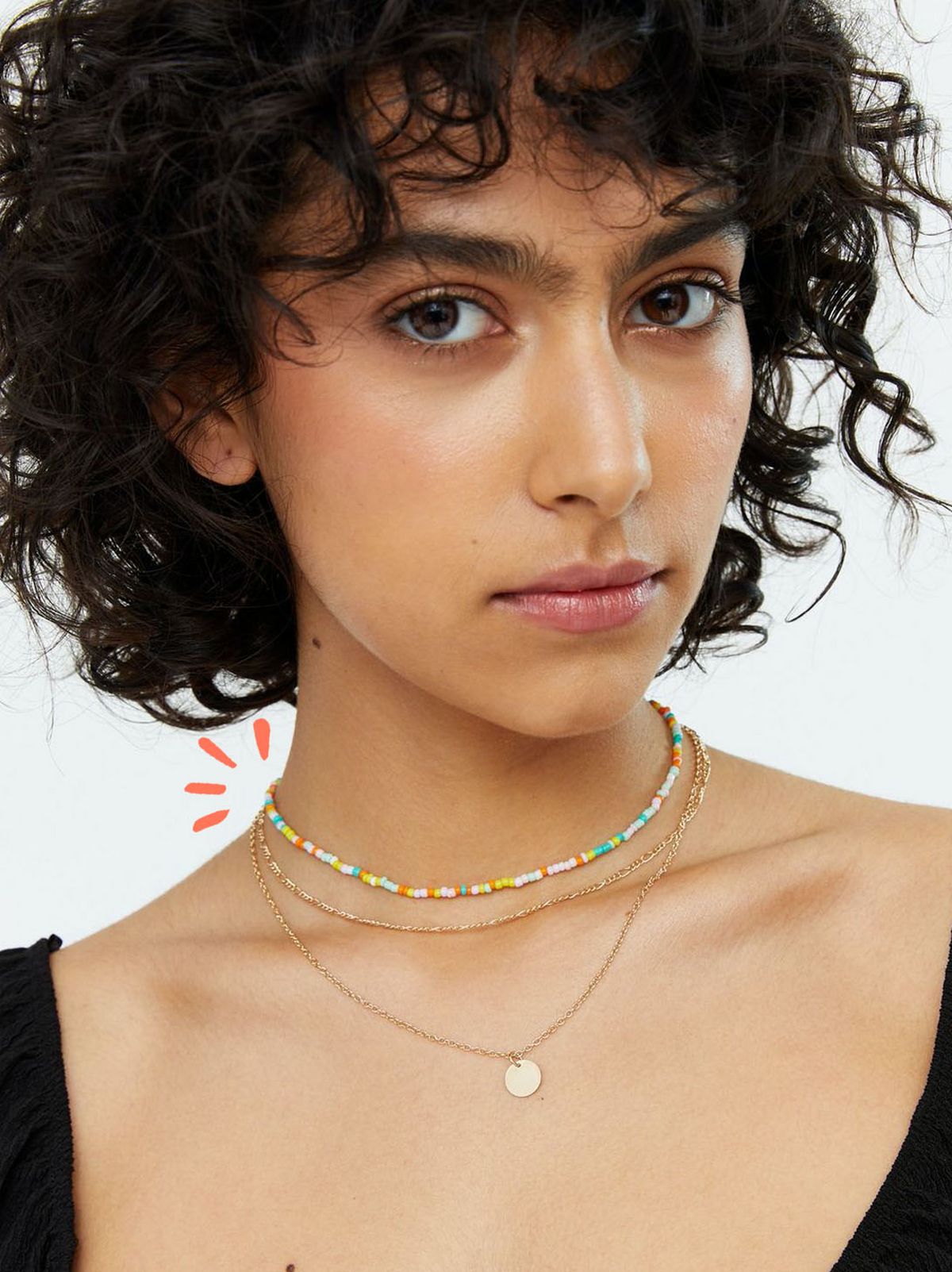 Woman wearing a gold disc pendant layered necklace and black top