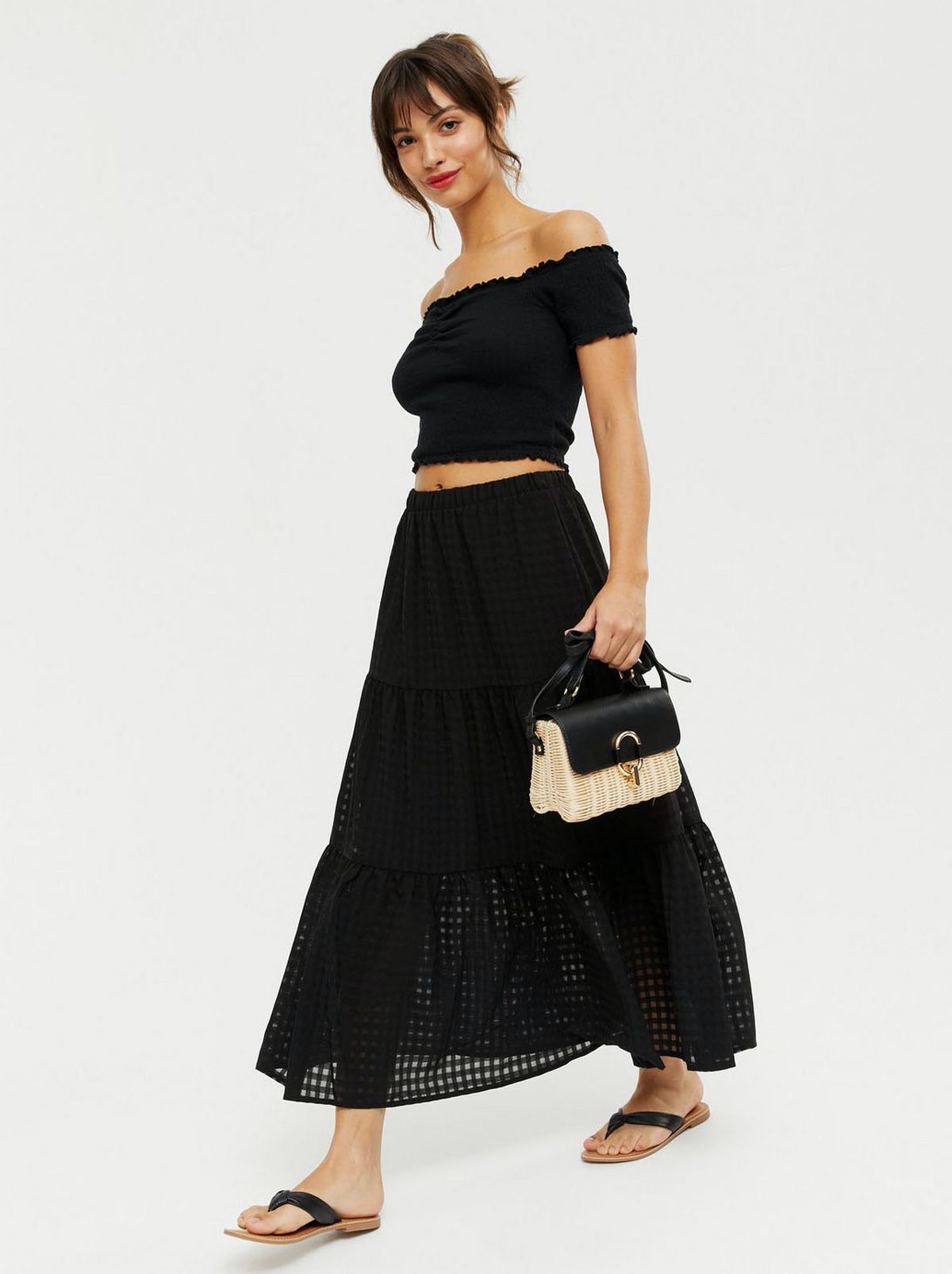 Woman wearing a black gingham high waist tiered midi skirt, black off shoulder top and sliders