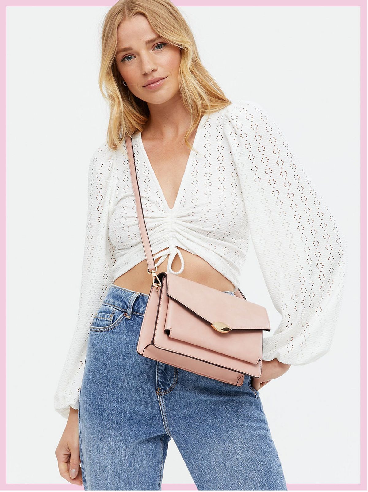 Woman wearing blue jeans, a white tie front jumper and pale pink cross body bag