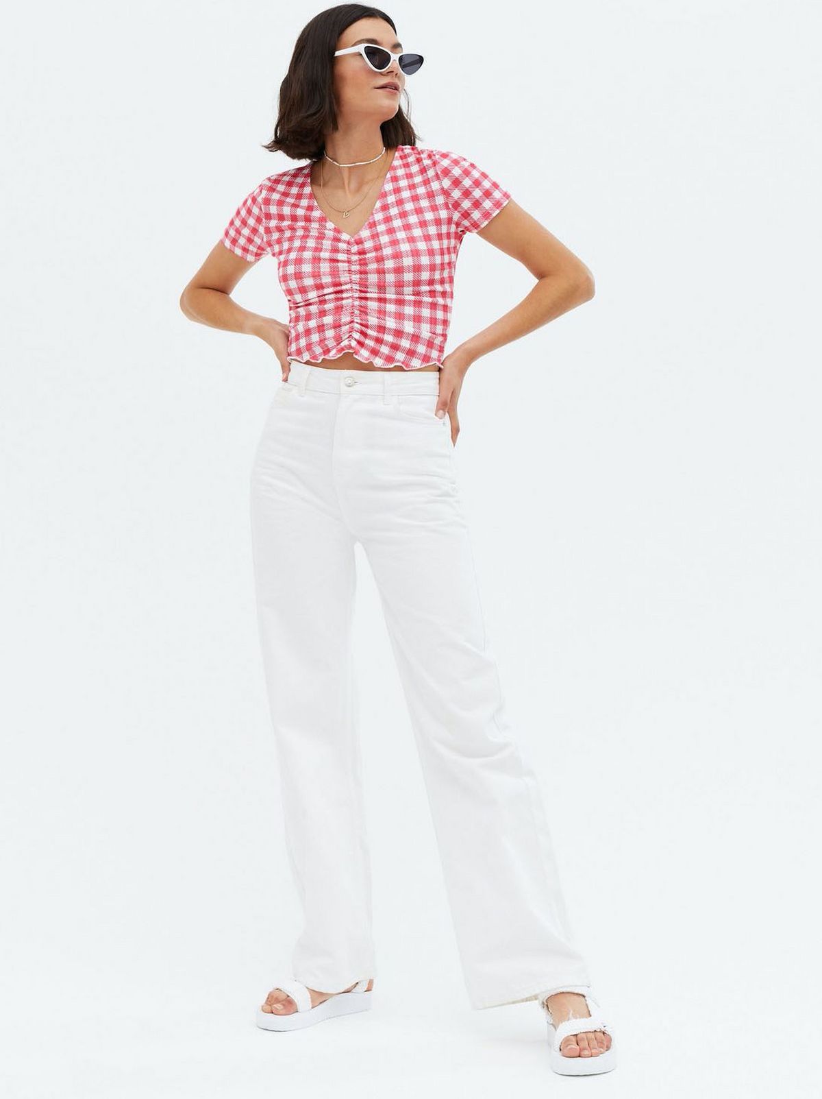 Woman wearing a red gingham ruched front top, white trousers and white sandals