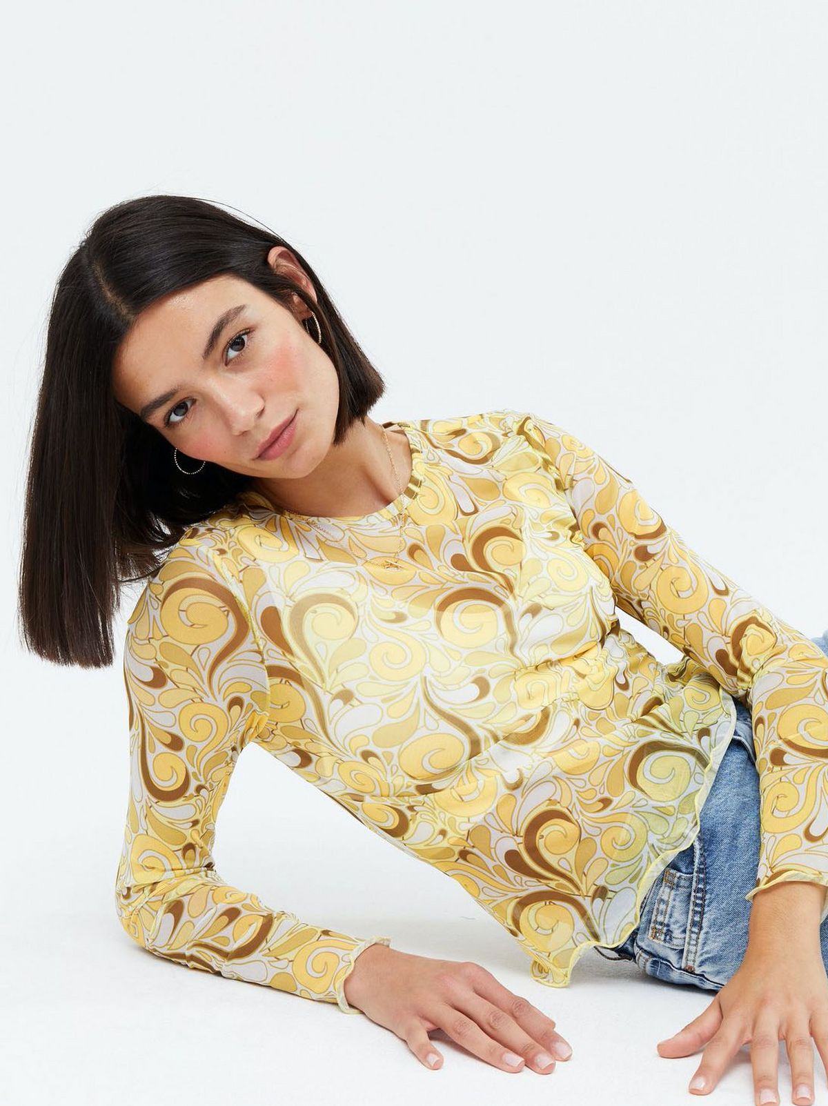 Woman wearing a yellow swirl mesh long sleeve top and blue jeans