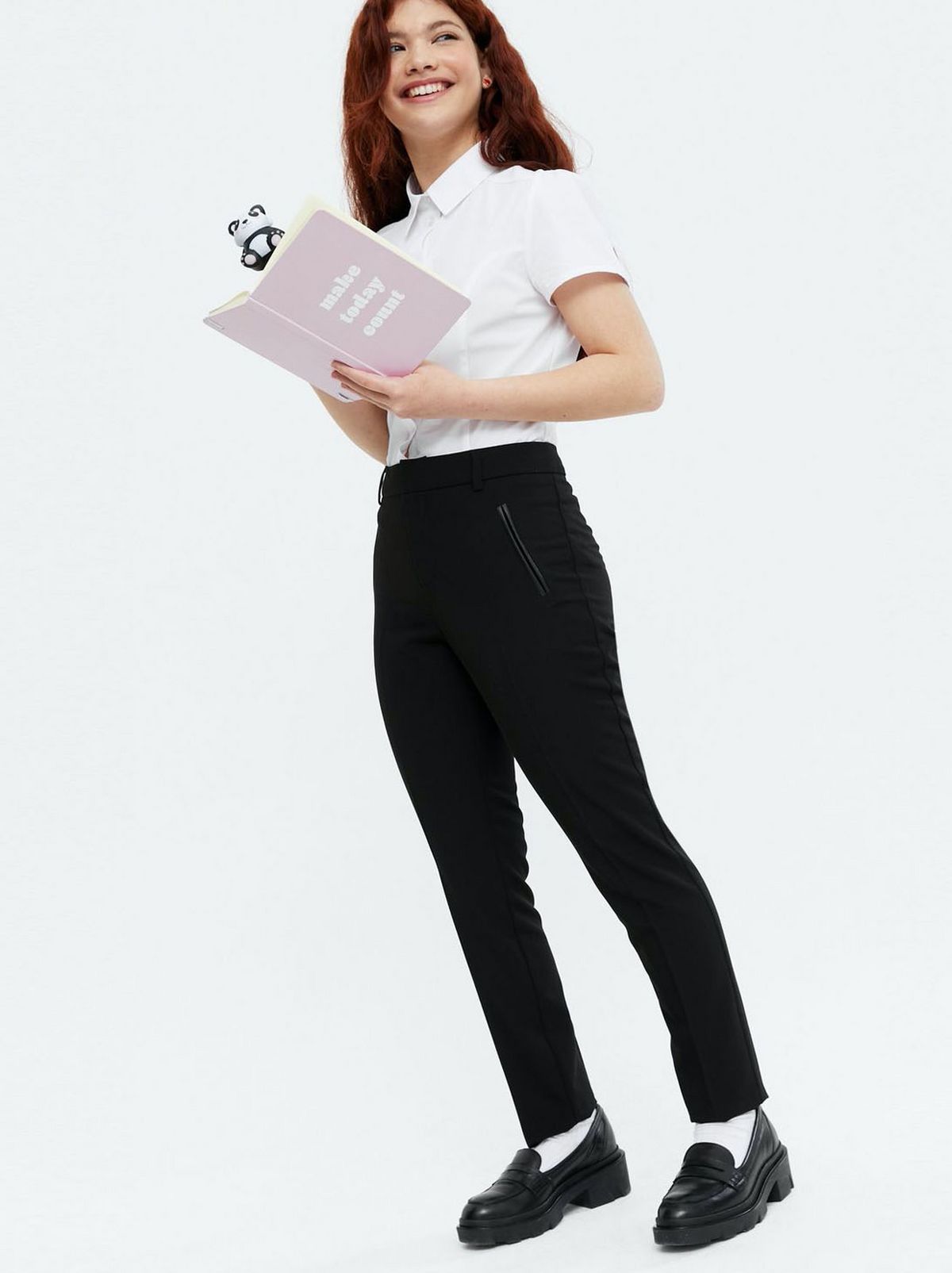 Girl wearing black high waist straight leg school trousers, a white shirt and black loafers