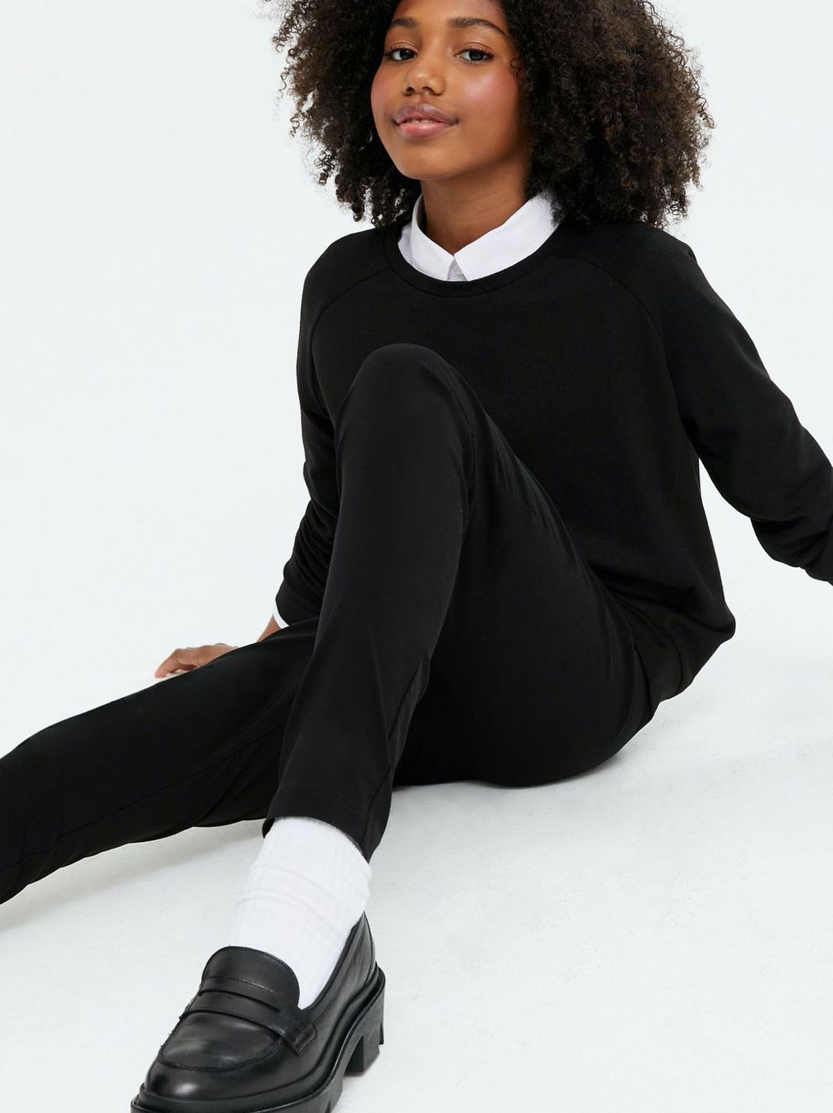 Girl wearing a black crew neck school jumper. black trousers and black shoes