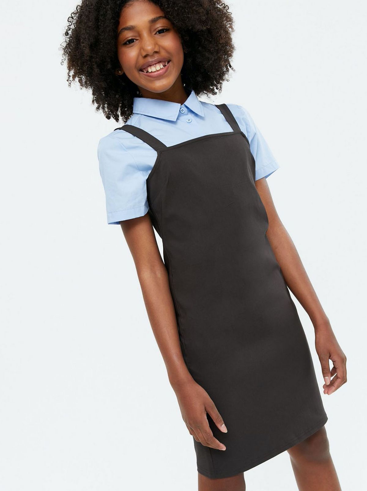 Girl wearing a dark grey school pinafore dress and blue collared shirt