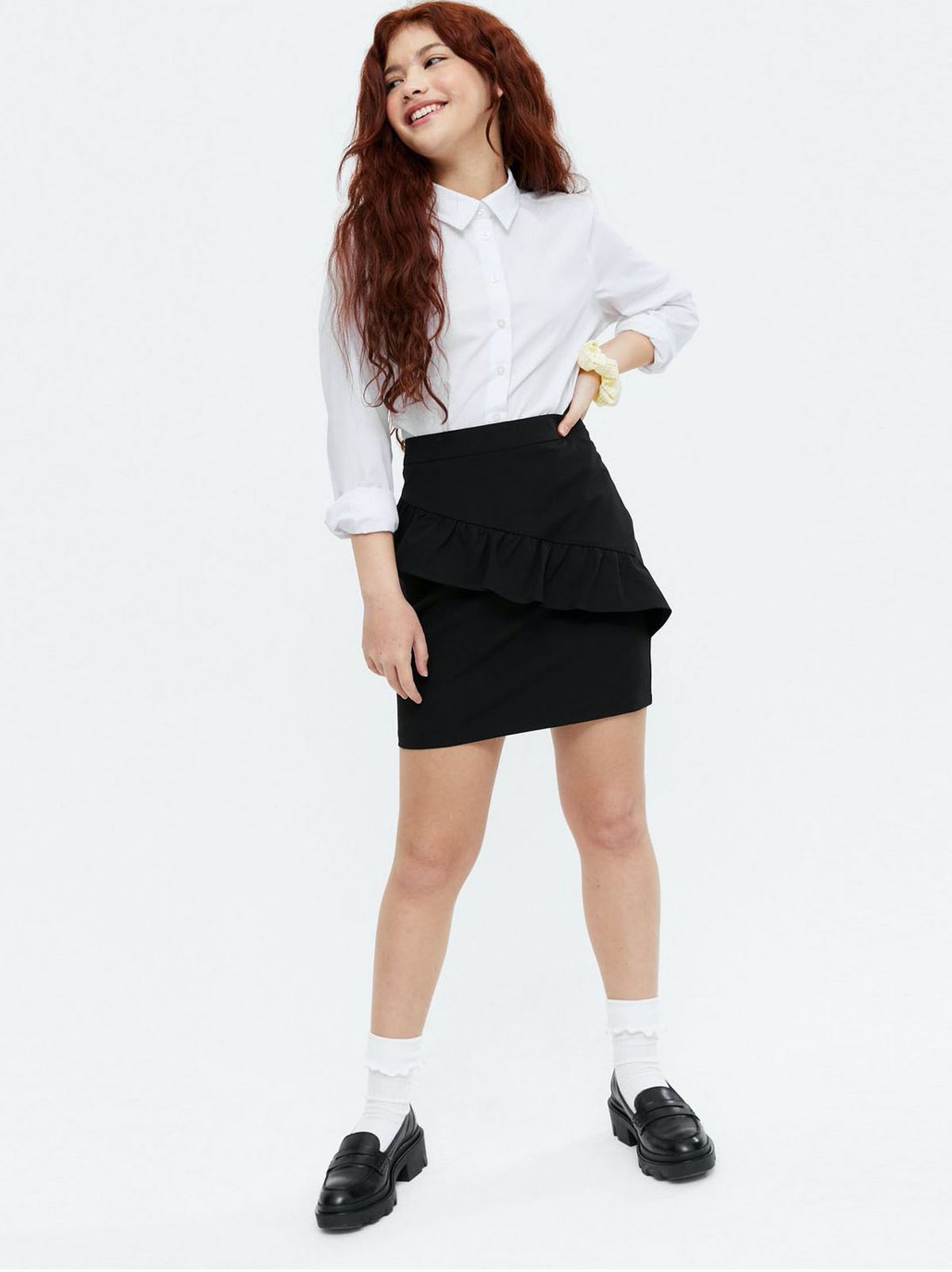 Girl wearing a black high waist ruffle school skirt, white shirt and loafers