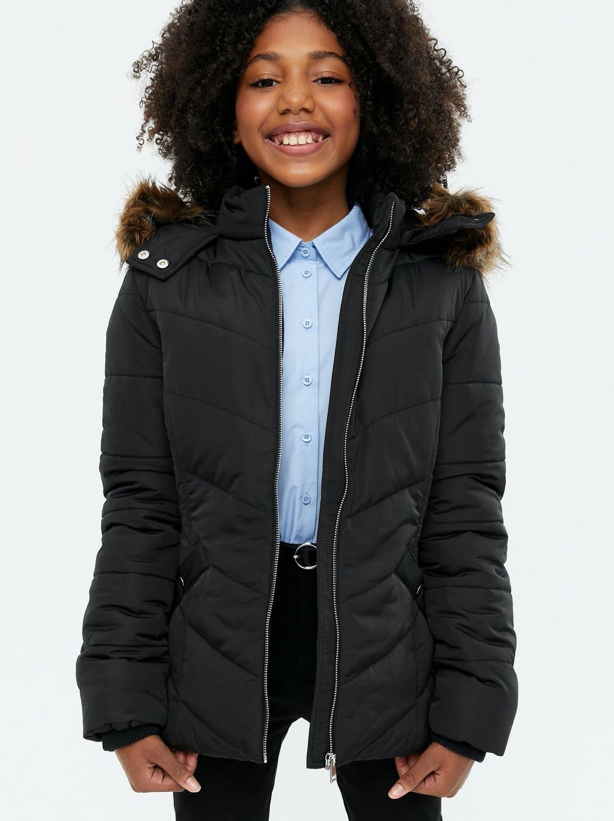 Girl wearing a black faux fur trim puffer jacket, blue shirt and black trousers