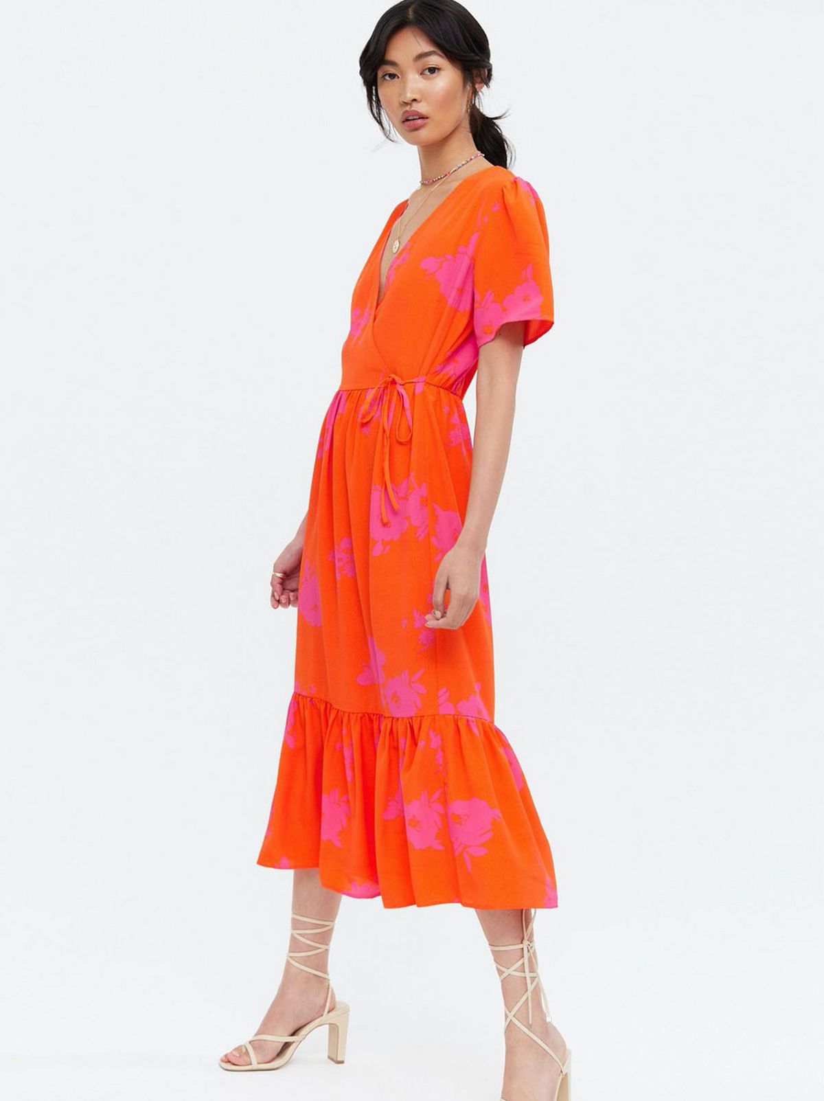 Woman wearing a orange floral wrap tiered midi dress and strappy heels