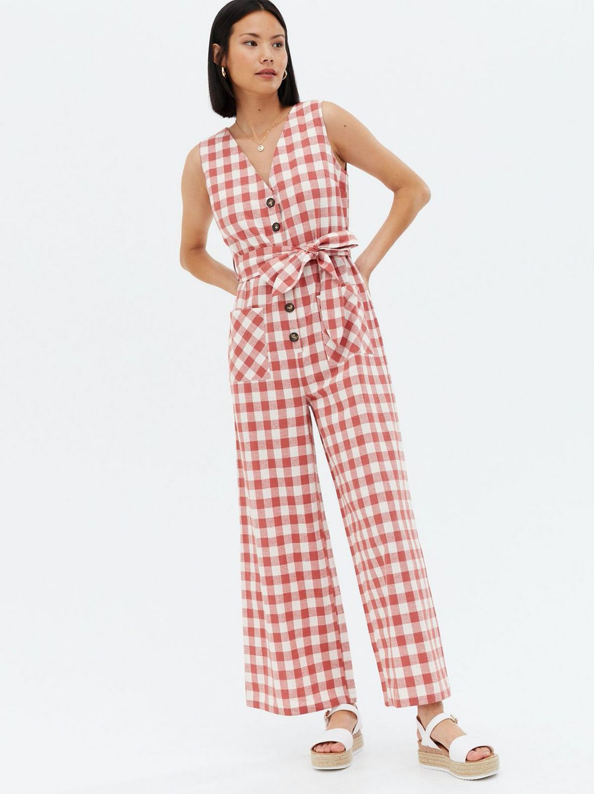 Woman wearing a red gingham belted jumpsuit and white chunky sandals