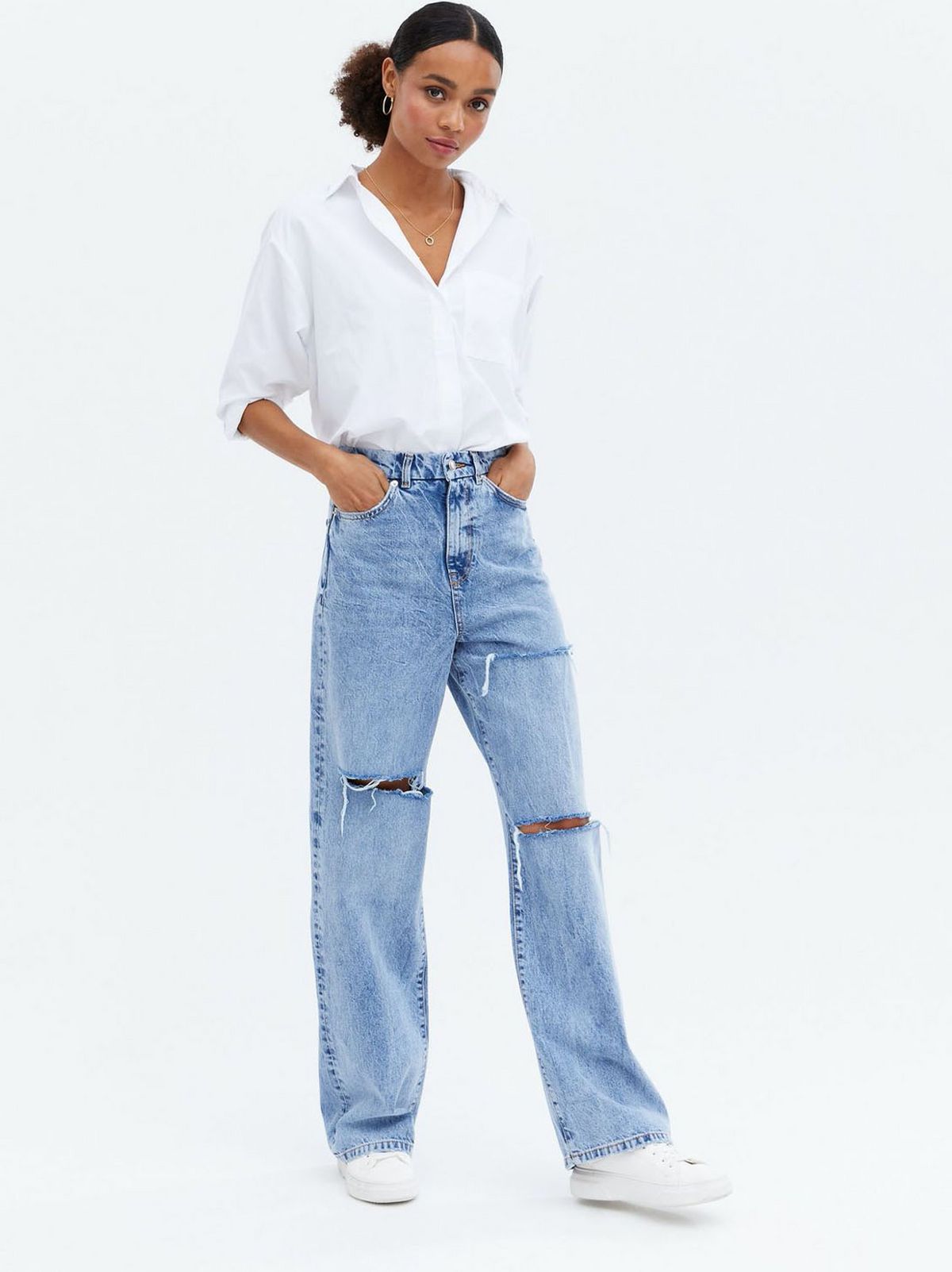 Woman wearing blue ripped knee 90s baggy fit jeans, a white shirt and trainers