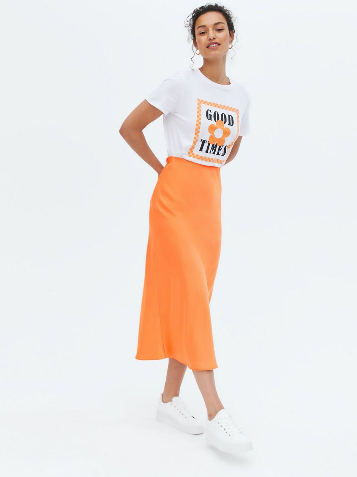 Woman wearing a bright orange satin midi skirt, white graphic t-shirt and trainers