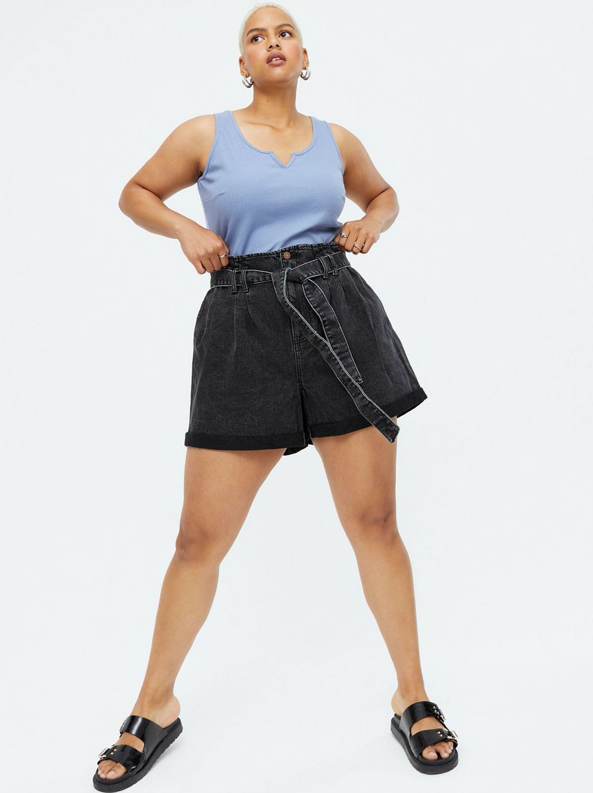 Woman wearing black denim high tie waist shorts, blue vest and black sandals