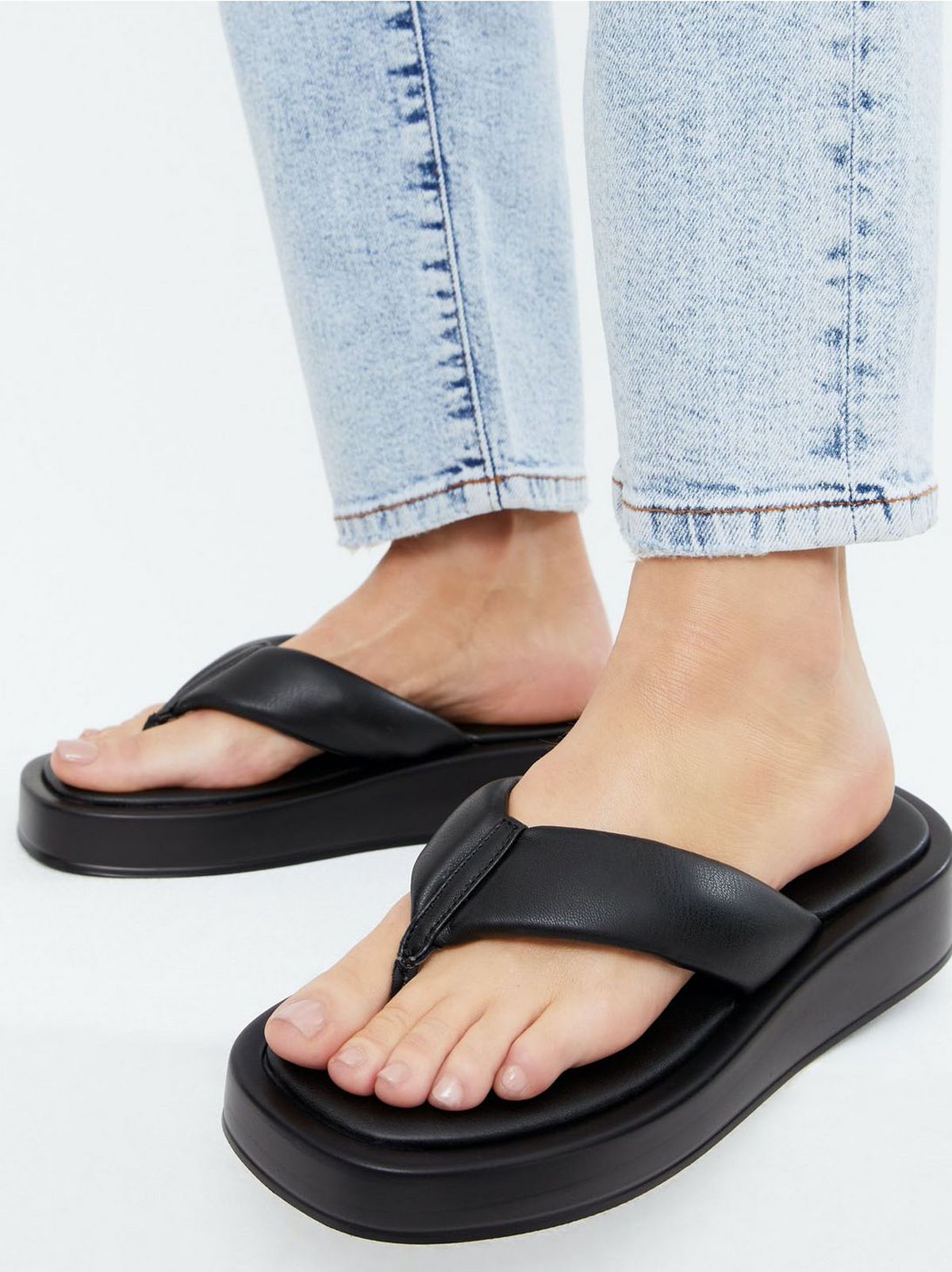 Woman wearing black leather look chunky flip flops and blue jeans