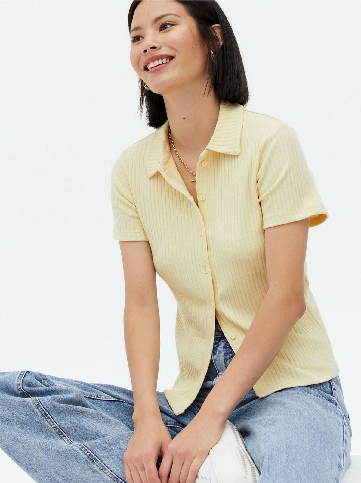 Woman wearing a pale yellow collared polo, jeans and white trainers