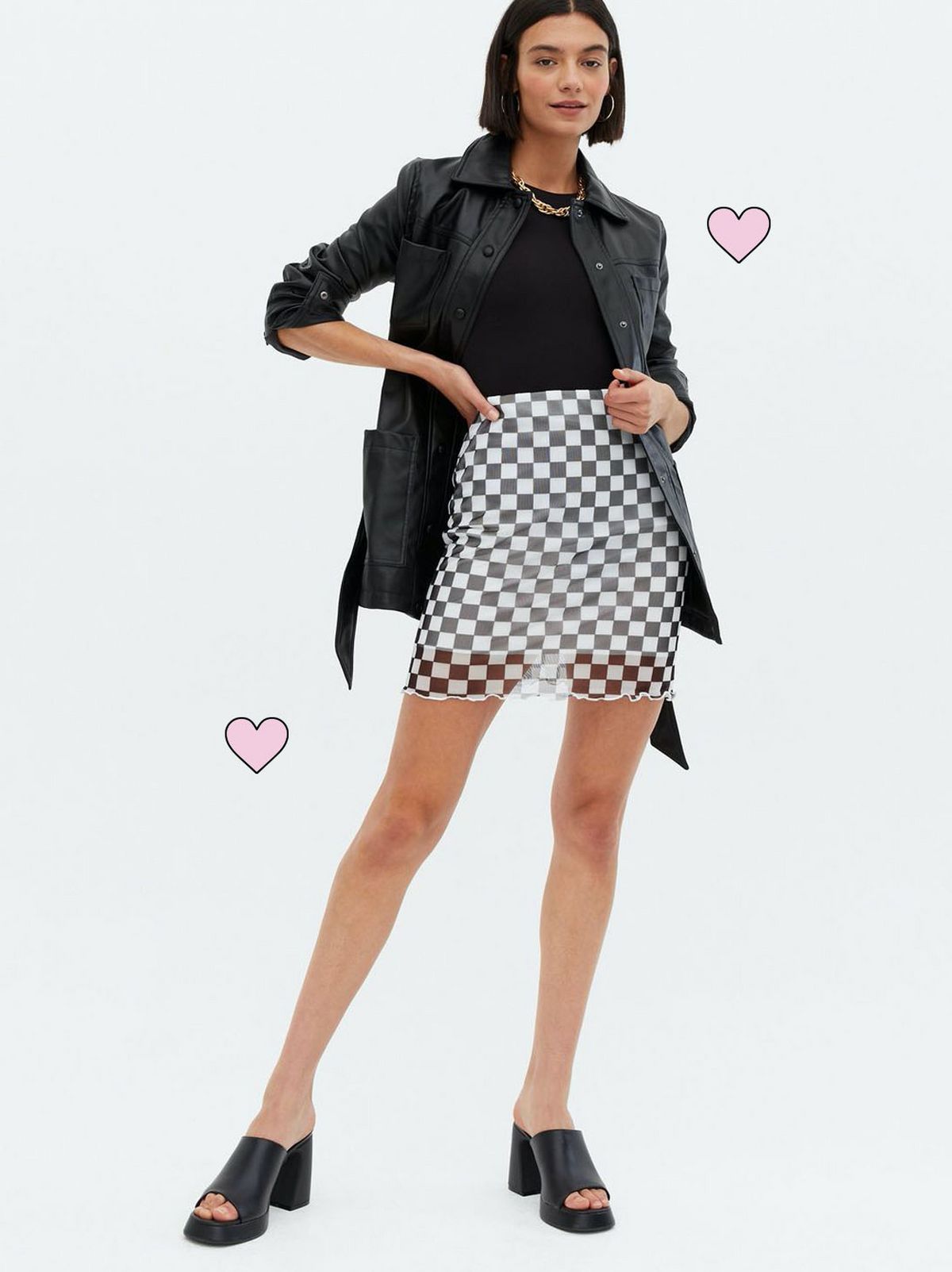Woman wearing a white checkerboard mesh frill tube skirt, black top and jacket with black heeled sliders