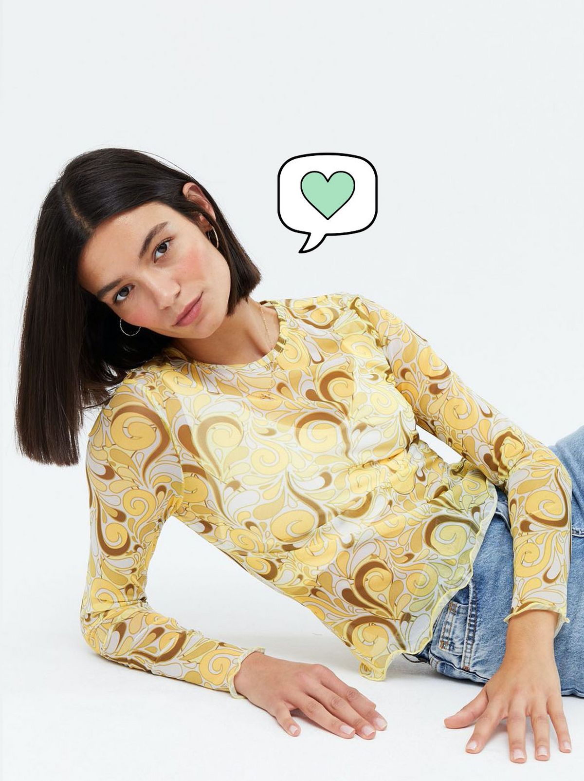 Woman wearing a yellow swirl mesh long sleeve top and blue jeans