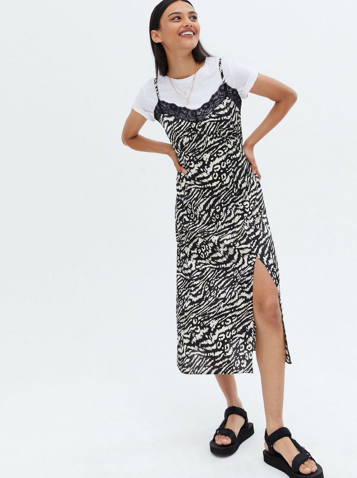 Woman wearing a black animal print satin spit hem midi dress with a white t-shirt and black sandals