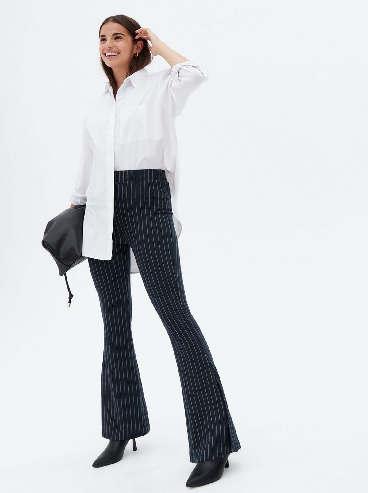 Woman wearing blue stripe jersey side split flared trousers, an oversized white shirt and black heels
