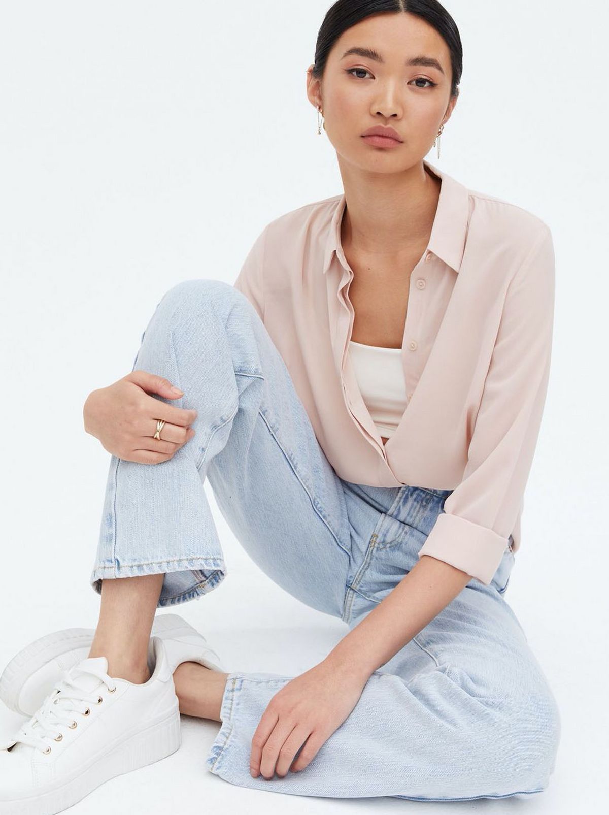 Woman wearing a pale pink long sleeve collared shirt, blue jeans and trainers