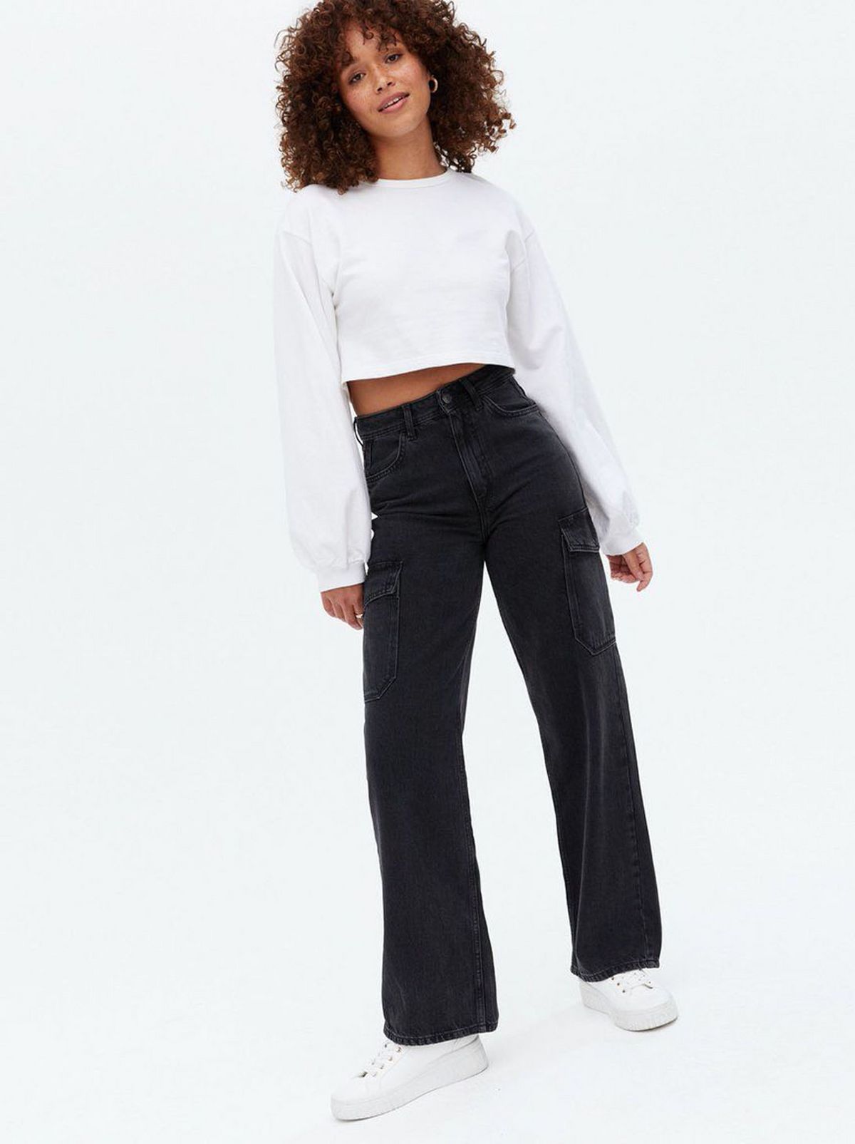 Woman wearing black cargo pocket 90s baggy fit jeans, white jumper and trainers