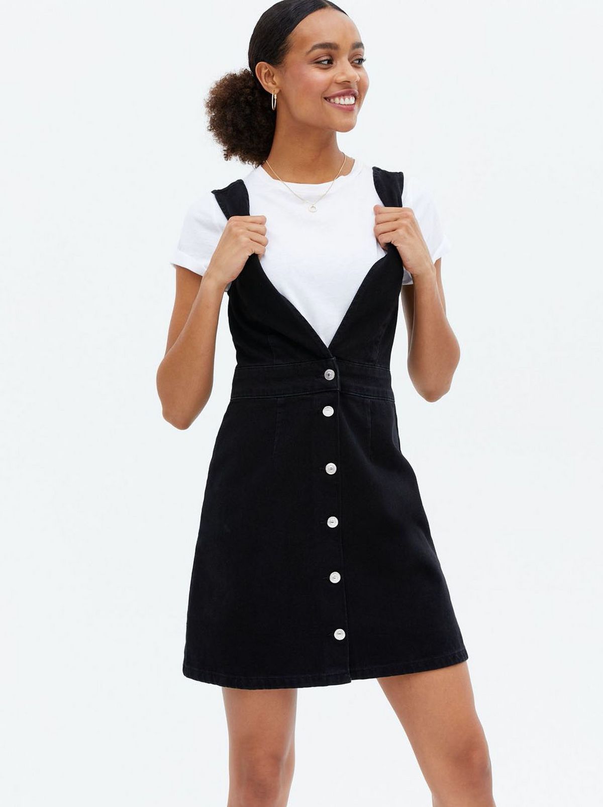 Woman wearing a black pinafore dress and white t-shirt