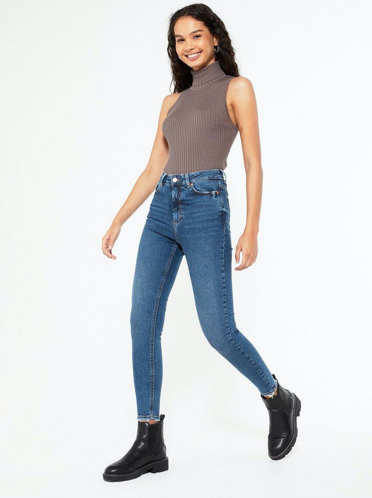 Woman wearing blue ripped skinny jeans, high neck sleeveless top and boots