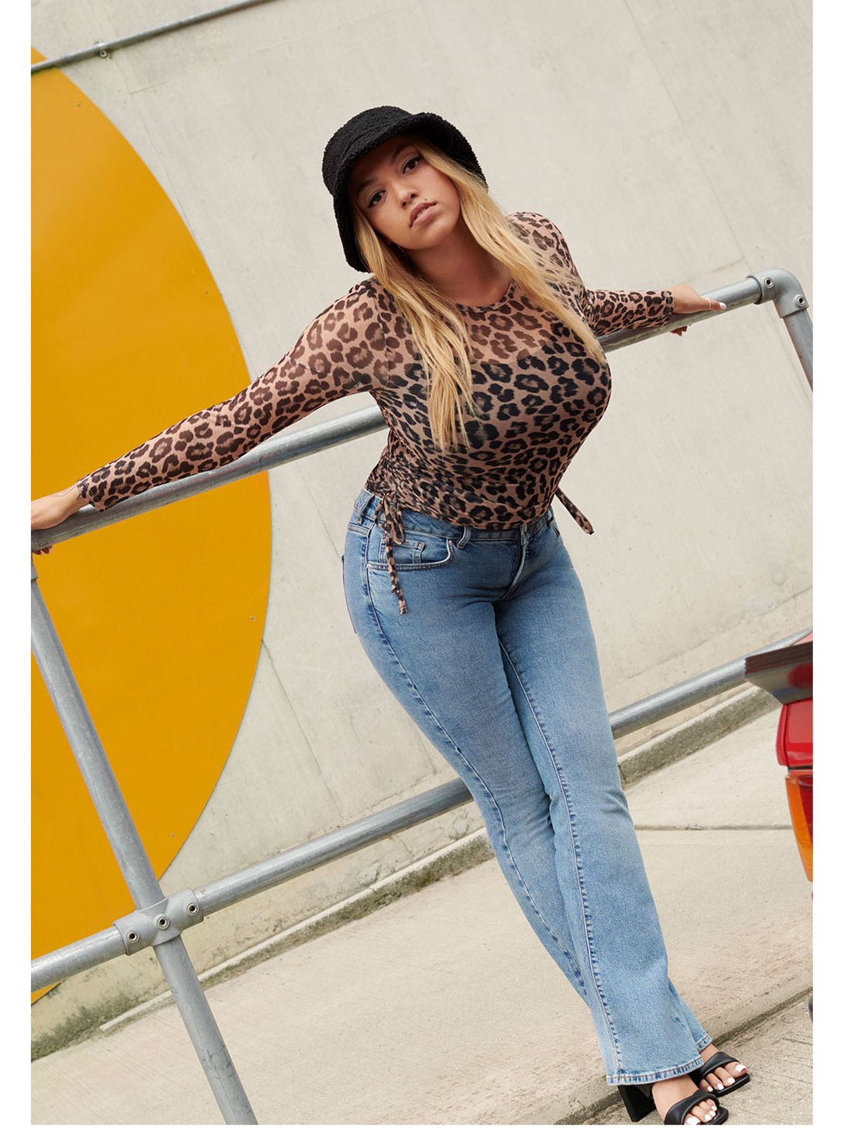 Mahalia wearing an animal print long sleeve top, blue jeans, heels and a black bucket hat