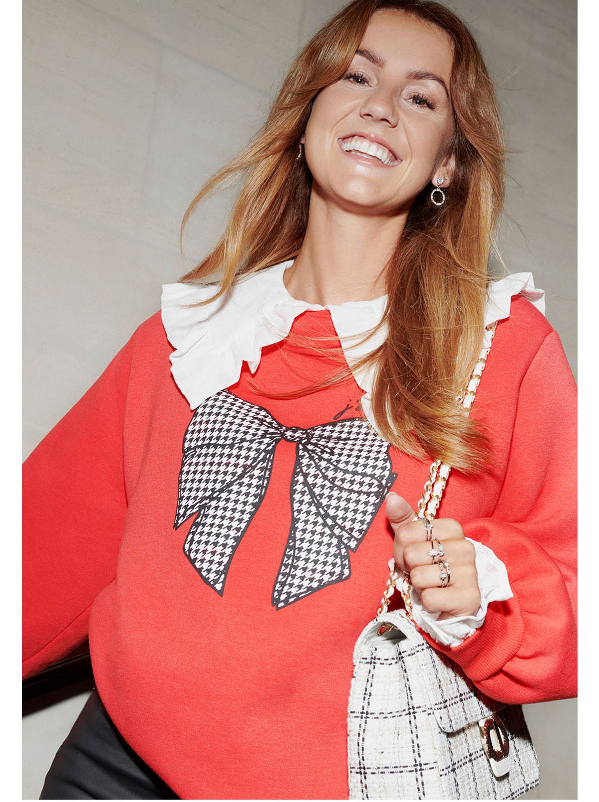 Laura Kennedy wearing a red graphic jumper with a white frill collar blouse carrying a checked handbag