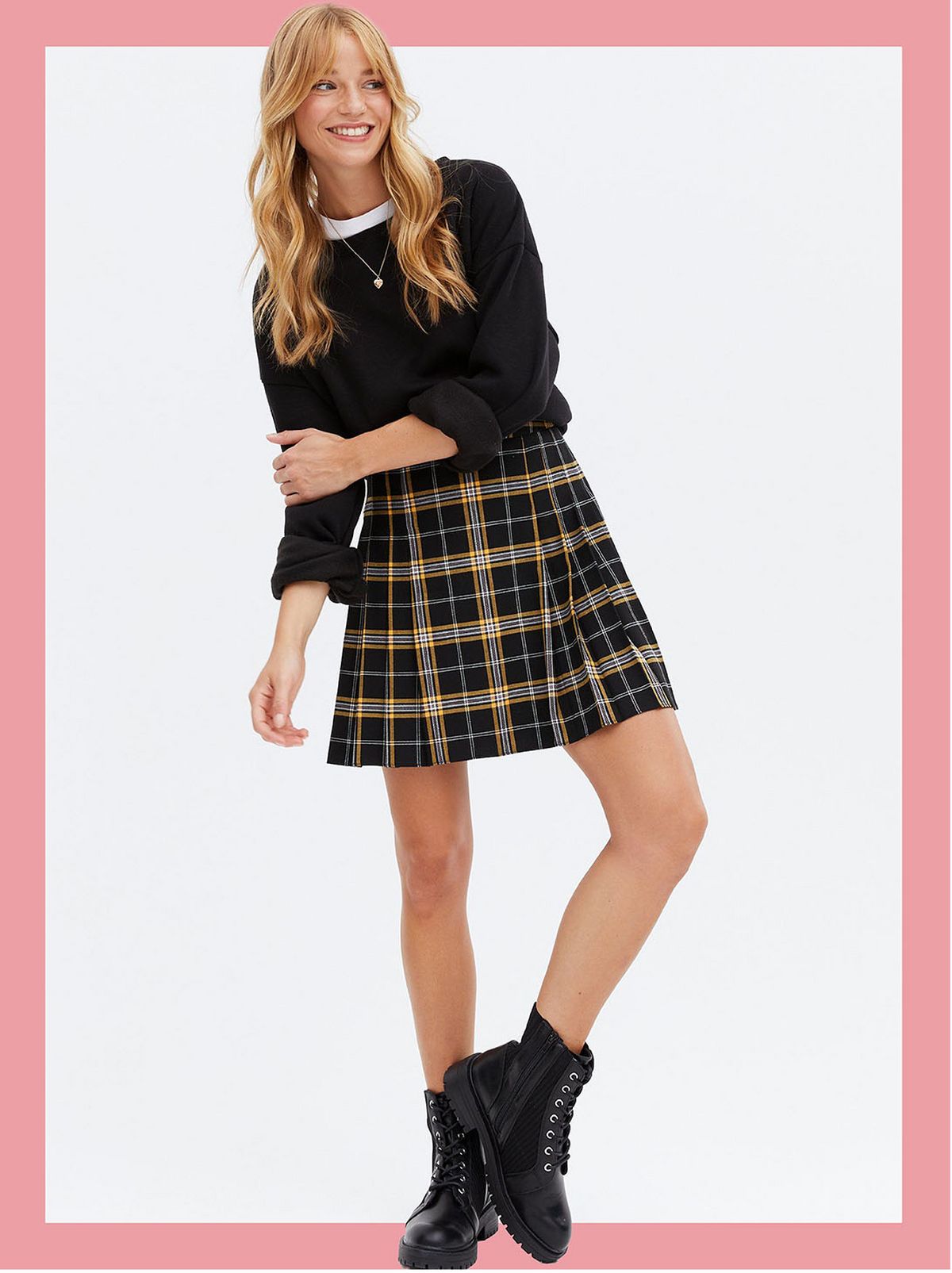 Woman wearing a black check high waist tennis skirt, black jumper and boots