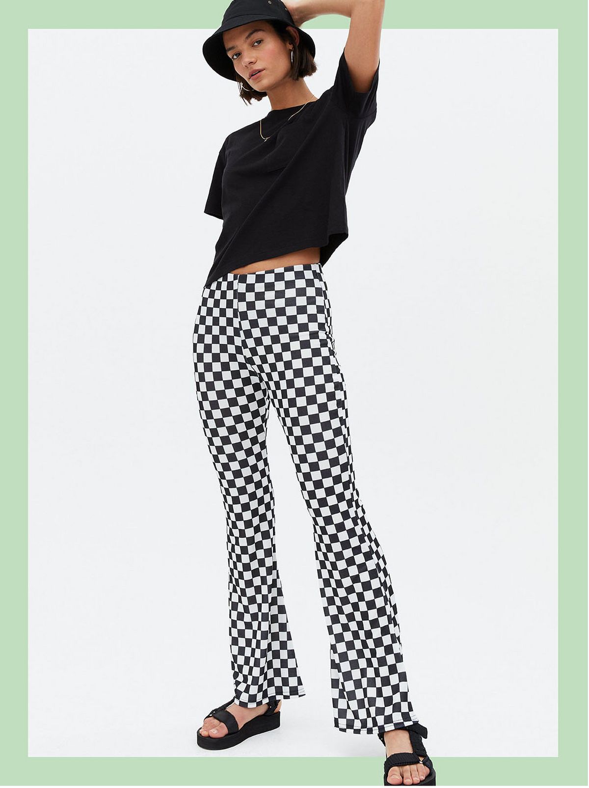 Woman wearing black checkerboard flared trousers, black t-shirt, sandals and bucket hat