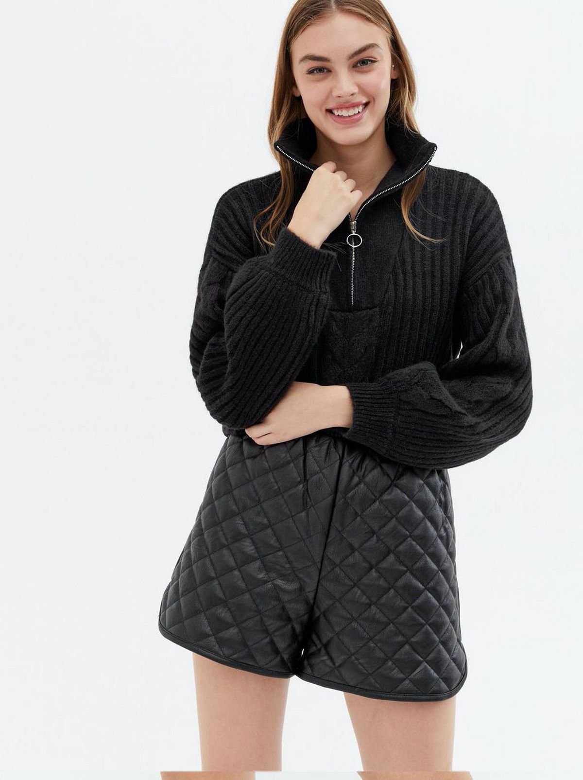 Woman wearing a black cable knit zip high neck jumper and quilted shorts