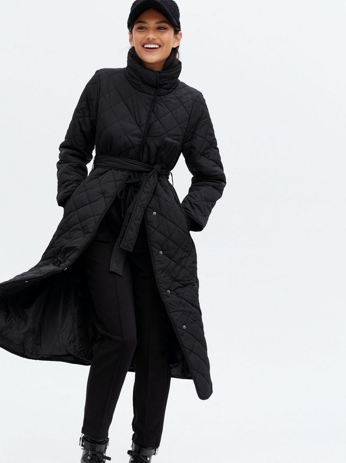 Woman wearing a black quilted high neck belted midi coat, black trousers and boots