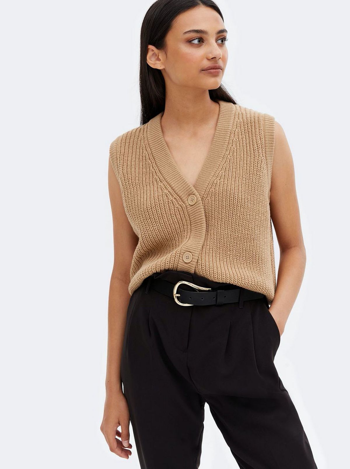 Woman wearing a camel ribbed knit button long sleeveless vest and dark brown trousers