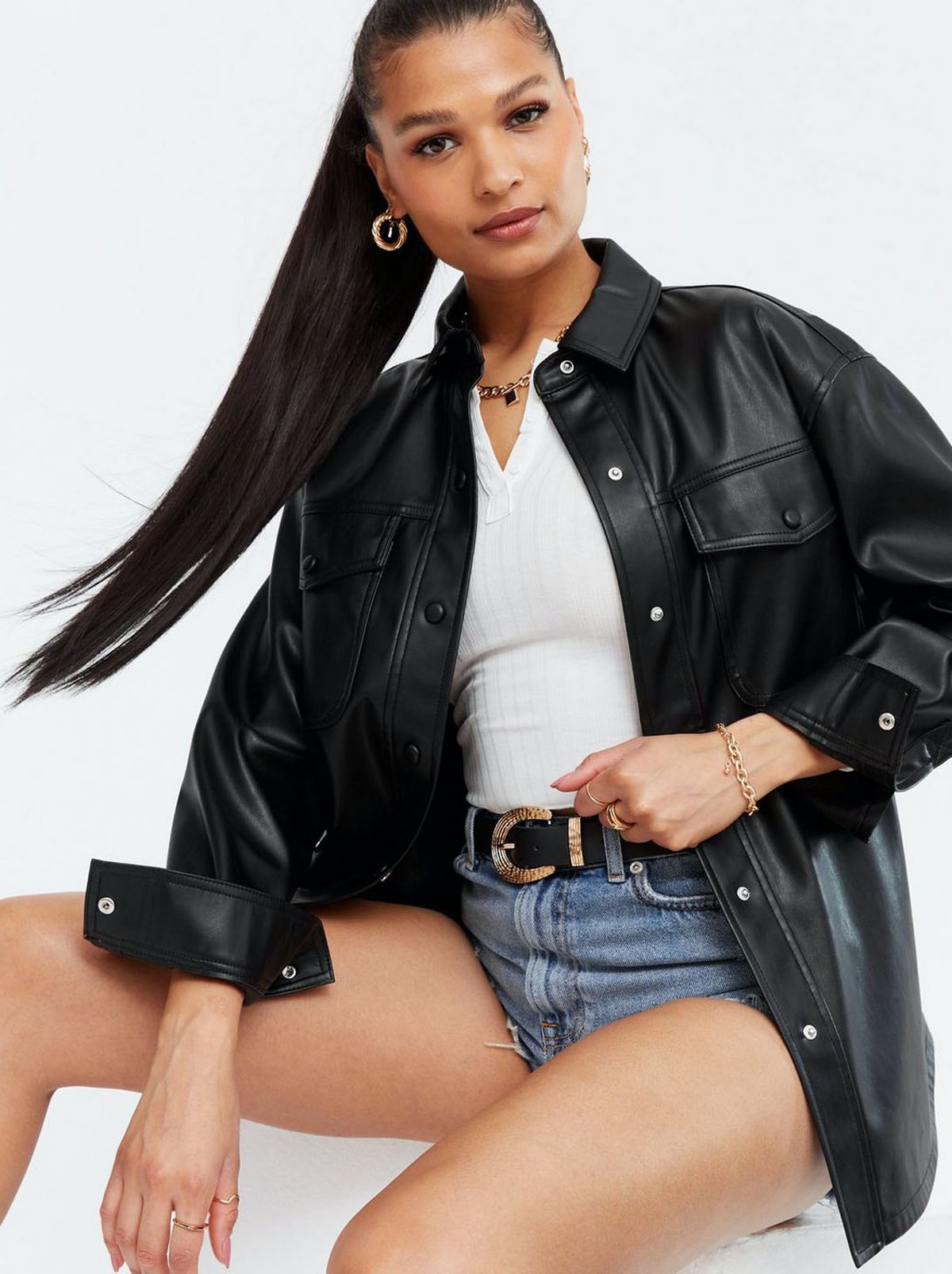 Woman wearing a black leather look shacket, white top and jean shorts